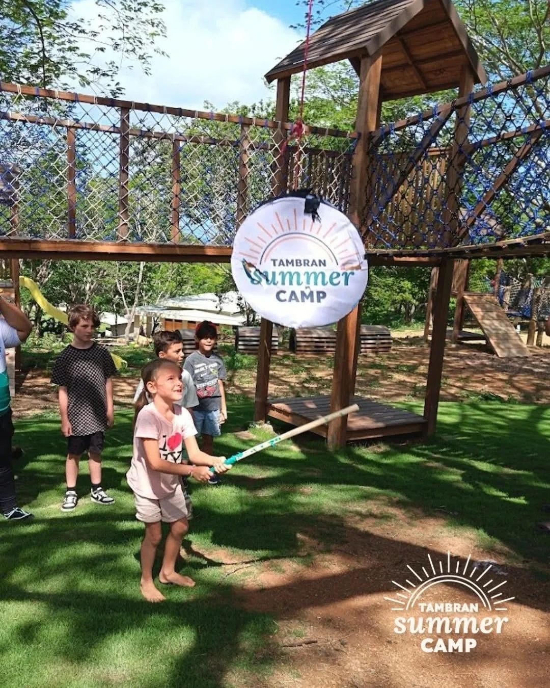 A girl swings at a piñata at Tambran Summer Camp while other kids wait their turn