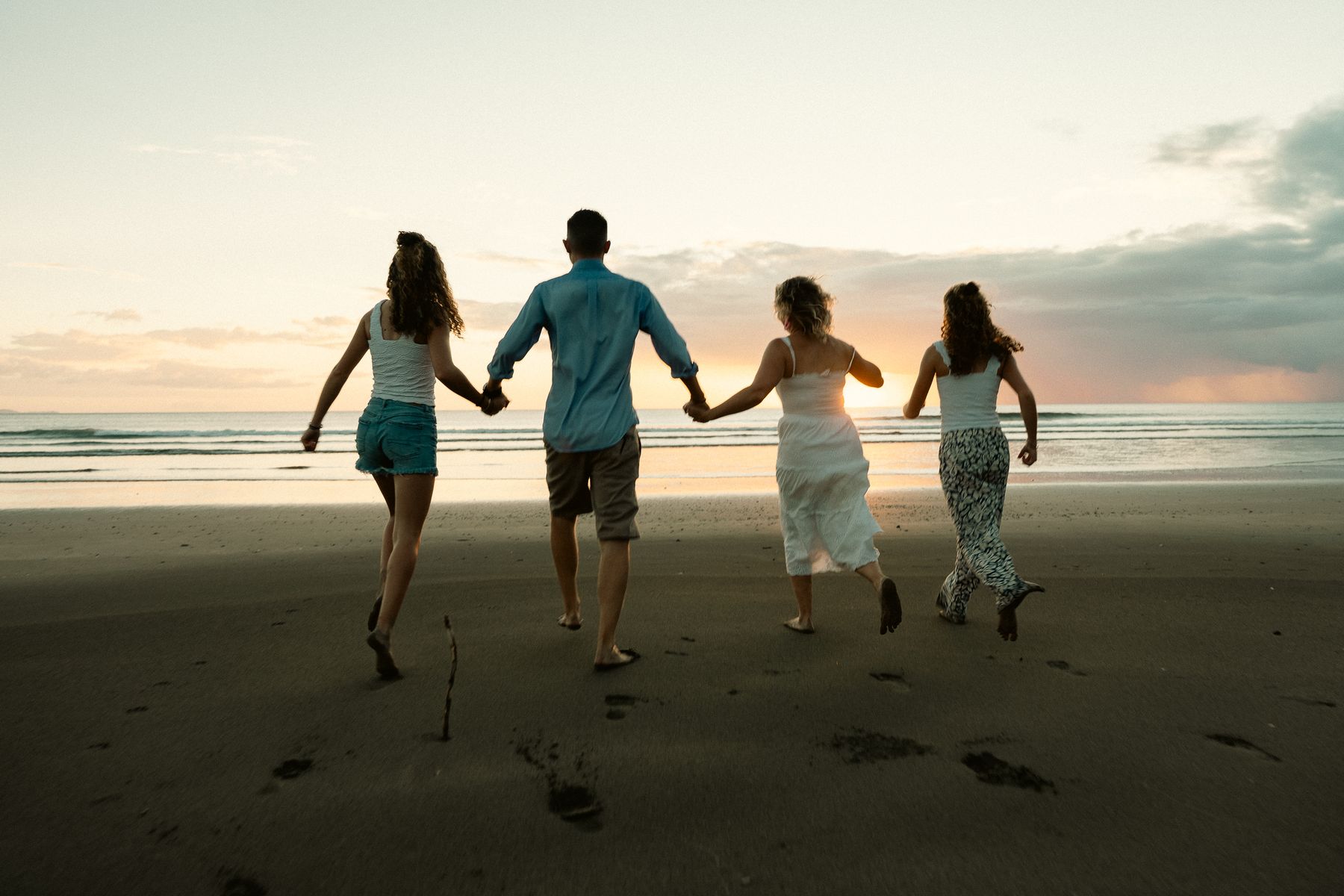 A family runs hand in hand toward the water at sunset