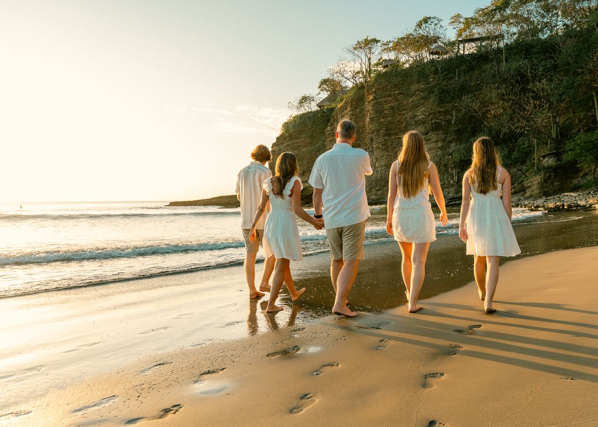 A family walks along the shore at golden hour, below the cliffs