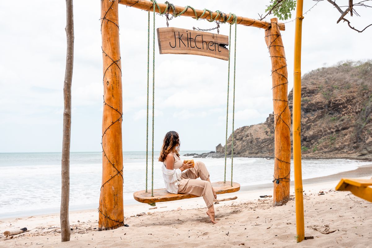 A woman sits on a wooden swing on the beach